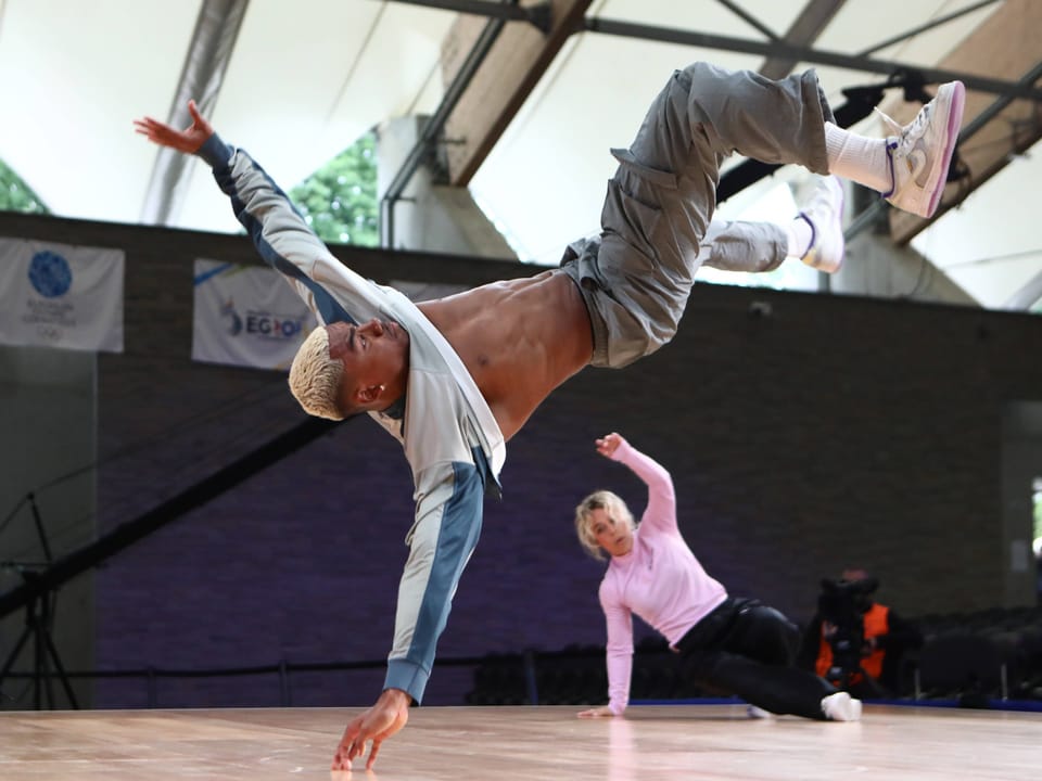 Tänzer führt Breakdance-Move aus, während eine andere Person im Hintergrund tanzt.