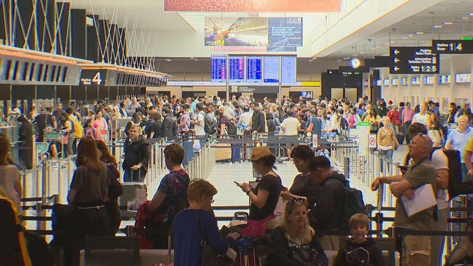 Menschen stehen am Flughafen Zürich vor den Check-in Schaltern an. 