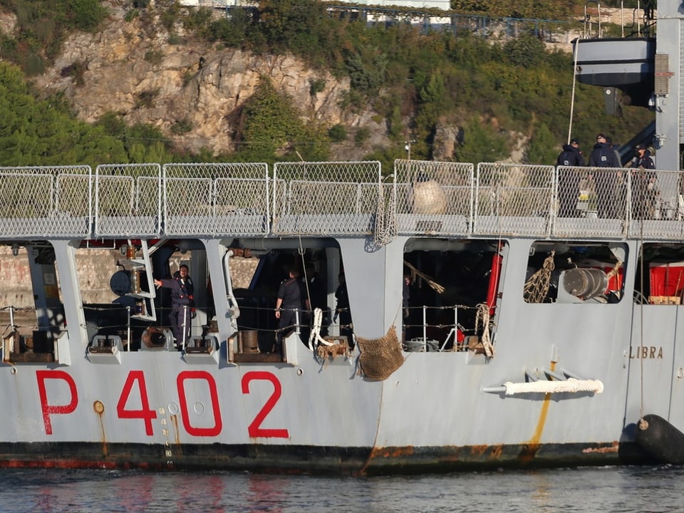 Graues Schiff P402 im Wasser, Küstenlandschaft im Hintergrund.