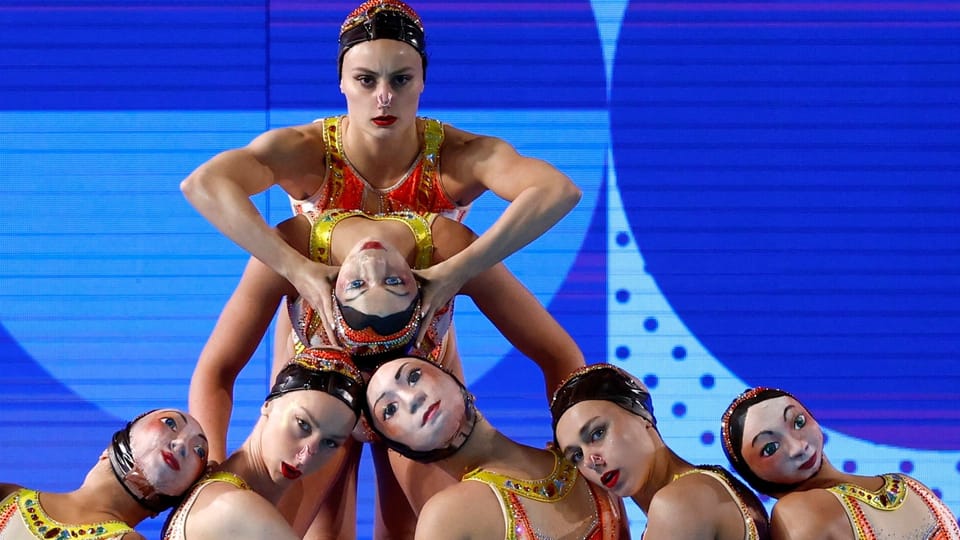 Frankreichs Synchronschwimmerinnen tragen Badekappen mit Gesichtsaufdrucken.