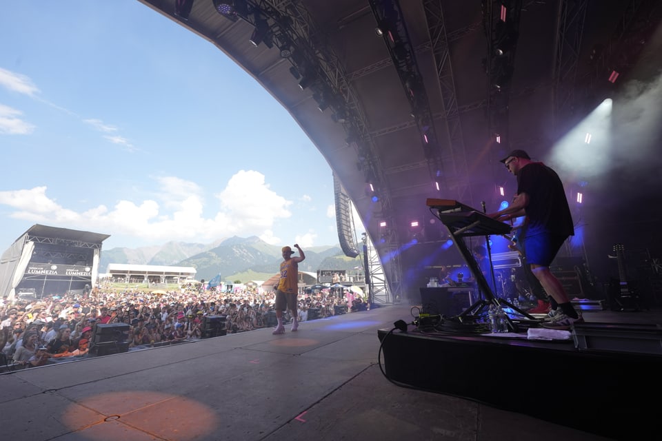 Konzertbühne mit Performer und Keyboarder, Menschenmenge im Freien am Open Air Lumnezia 2024.