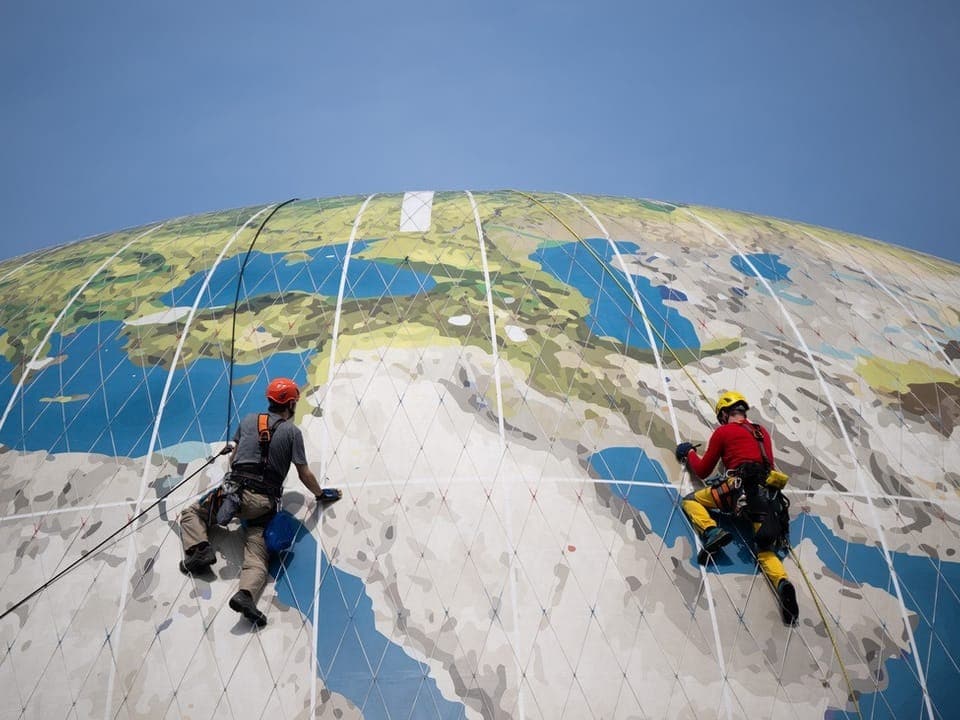 Two workers climb a huge globe.