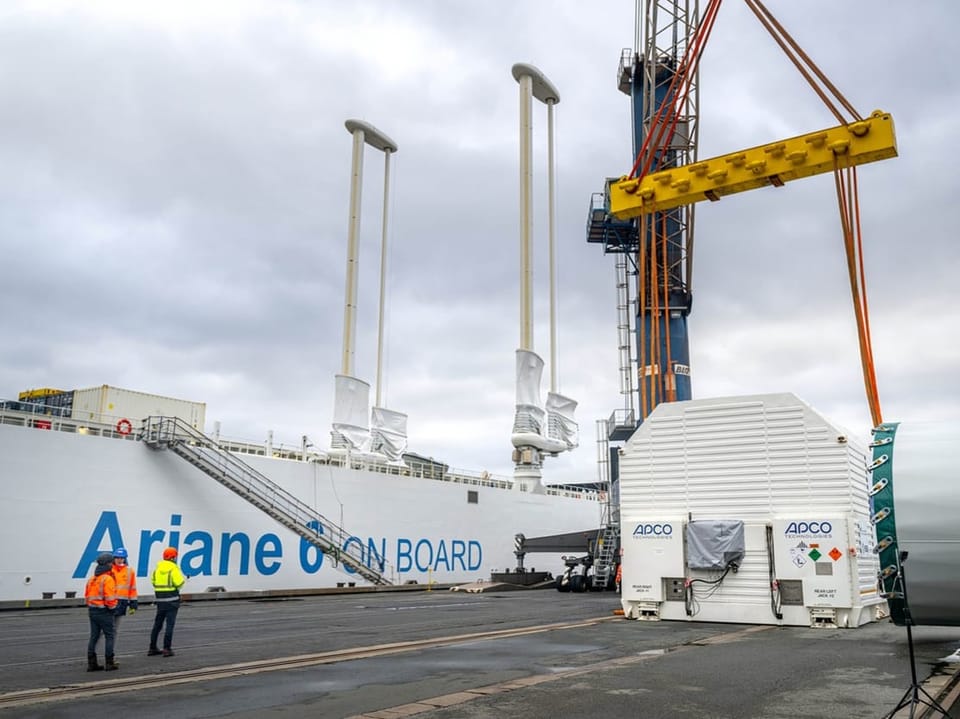 Zwei Personen vor einem Schiff mit der Aufschrift 'Ariane on Board'.