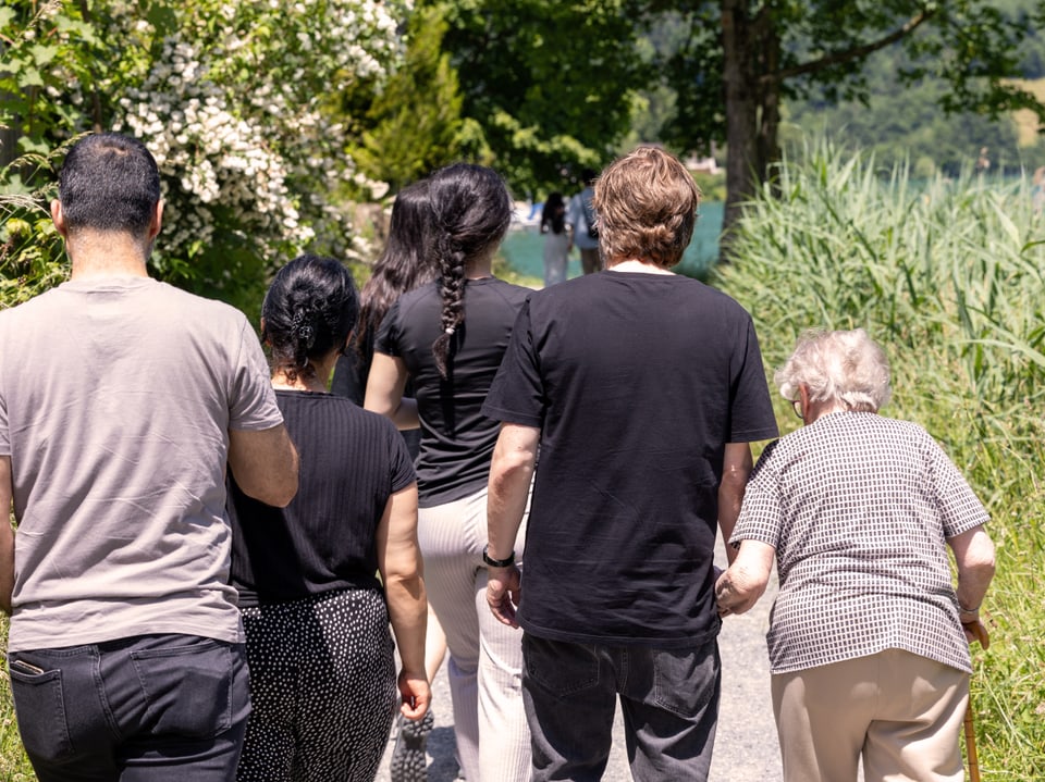 Eine Gruppe von Leuten von hinten fotografiert. Sie laufen auf einem Kiesweg entlang des Sees.