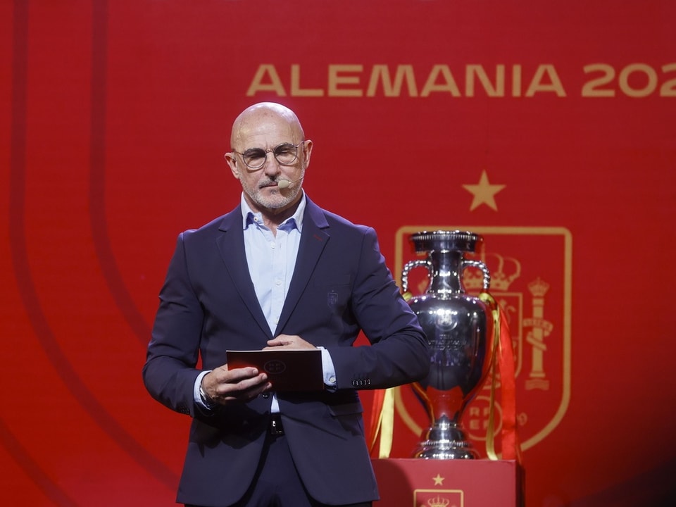 Mann in Anzug und Brille mit Pokal im Hintergrund.