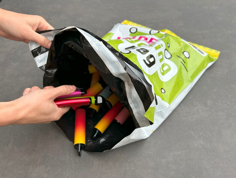 Hand deponiert Vapes in einem Recycling-Sack.