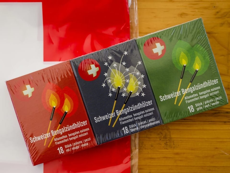 Drei Schachteln mit bengalischen Zündhölzern liegen auf einer Schweizerfahne.