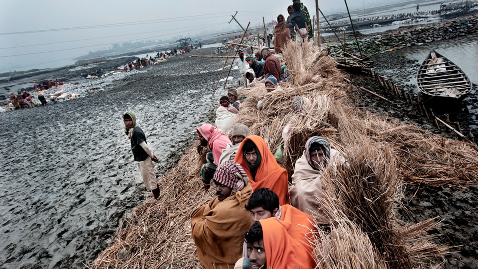 Leute in Bangladesch sitzen zusammengepfercht sind verhüllt auf einem Lehmhaufen.