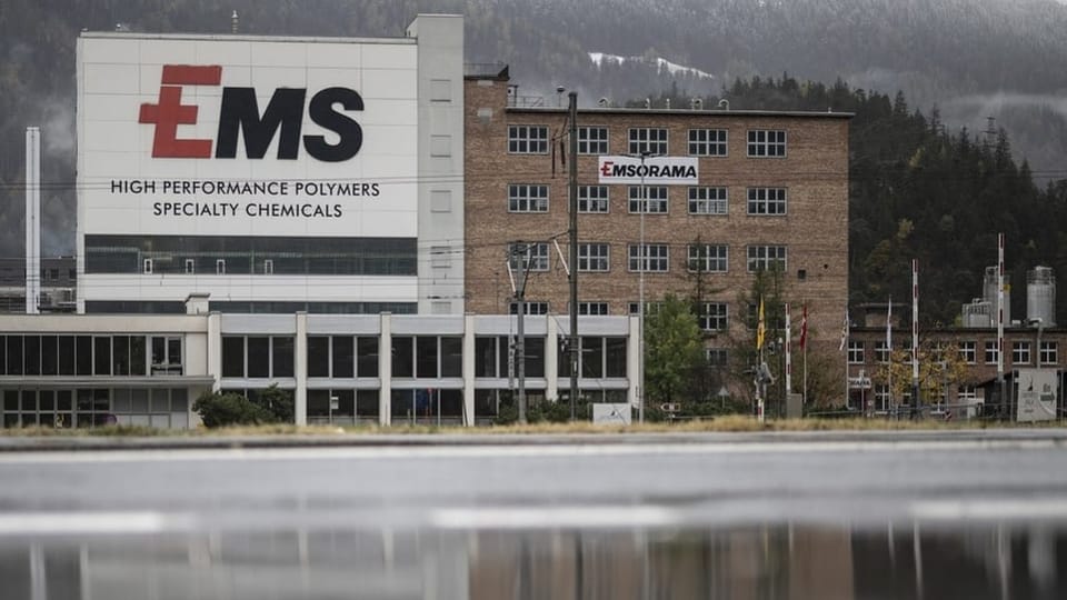 Industriegebäude mit EMS-Logo und Bergen im Hintergrund.
