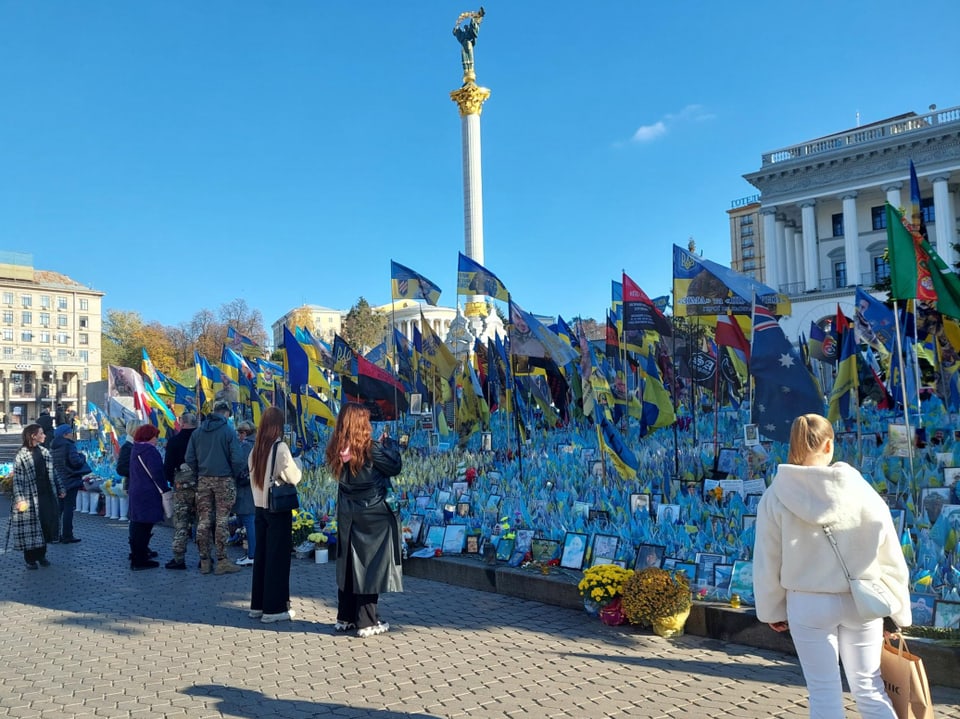 Menschen betrachten Flaggen und Gedenktafeln auf dem Maidan in Kiew.