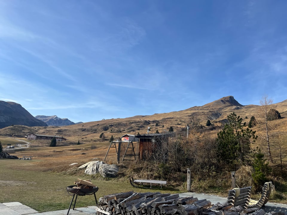 Landschaft mit Wiese, Bergen im Hintergrund und Holzkohlegrill.