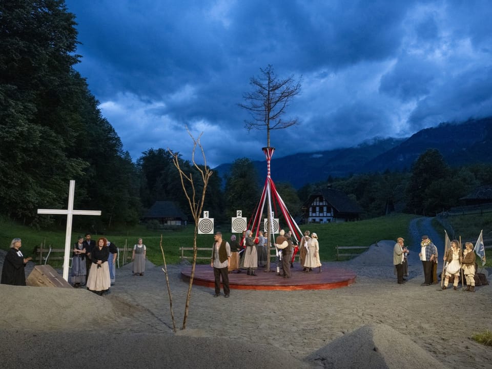 Schauspielende, ein dürrer Baum steht im Zentrum, dahinter ein grosses Kreuz