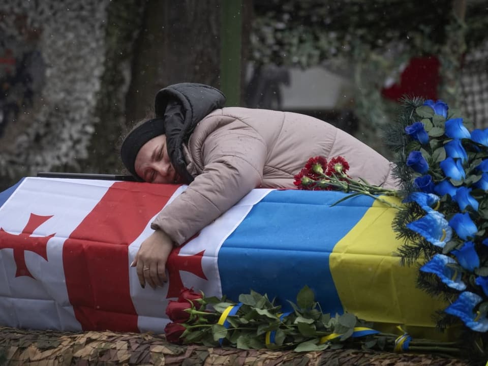 Eine Frau umarmt in Trauer einen Sarg umhüllt mit Georgischen und Ukrainischen Flaggen.