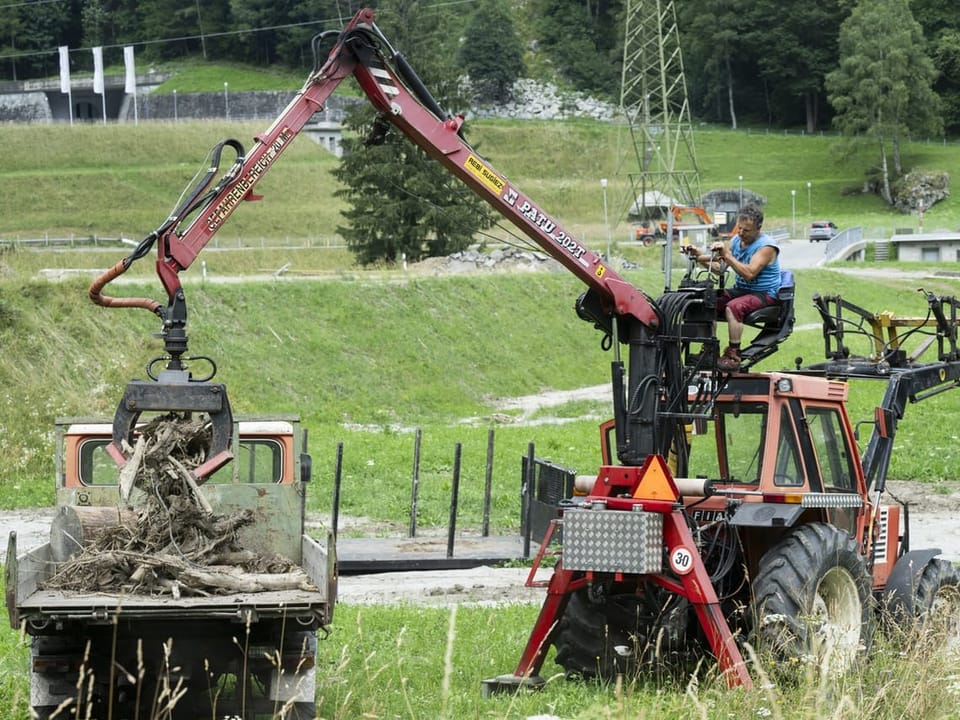 Mann fährt einen Traktor mit Kran und lädt Holz auf einen Anhänger.