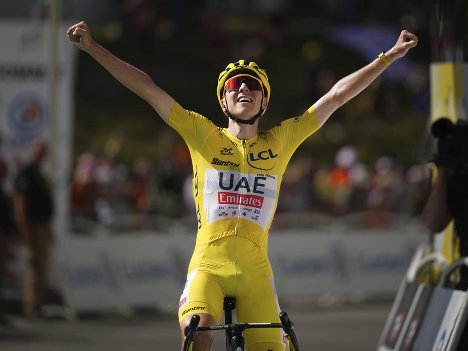 Radrennfahrer in gelbem Trikot jubelt mit erhobenen Armen im Ziel.