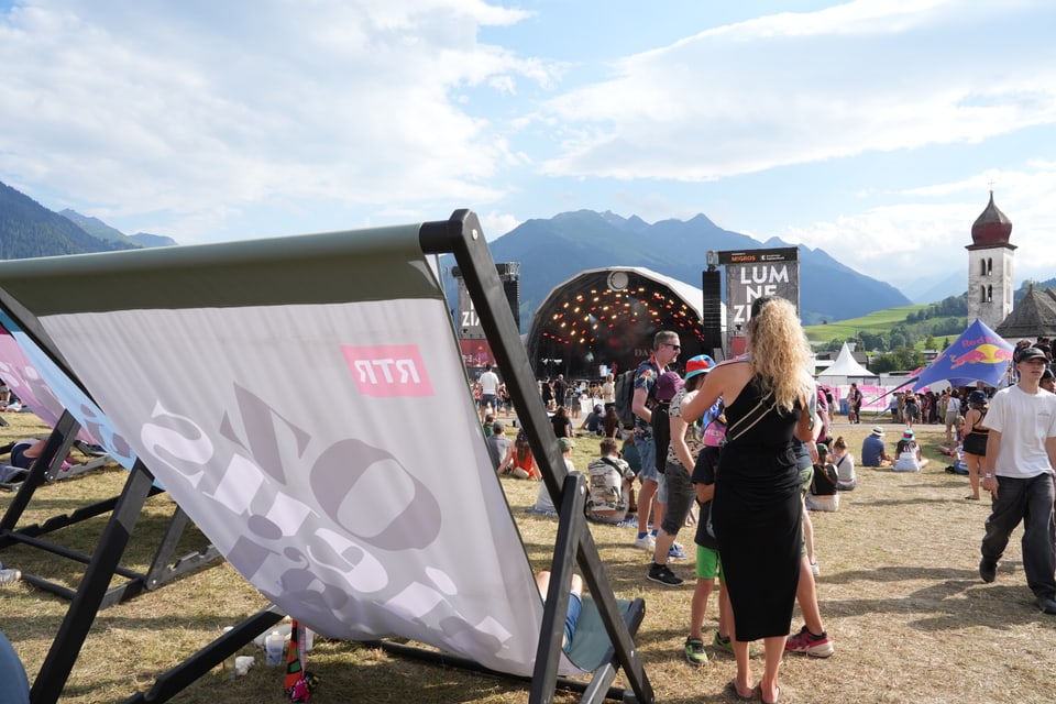 Outdoor-Musikfestival mit Bühne und Menschenmengen bei sonnigem Wetter.