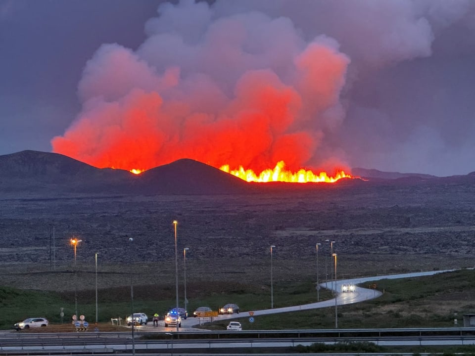 Vulkaneruption mit Lava und Rauch in der Ferne, Strasse im Vordergrund.