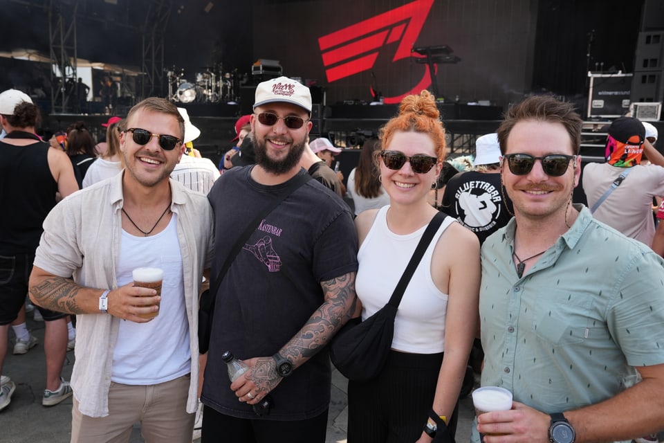 Vier Personen auf einem Musikfestival, Bühne im Hintergrund am Open Air Lumnezia 2024.