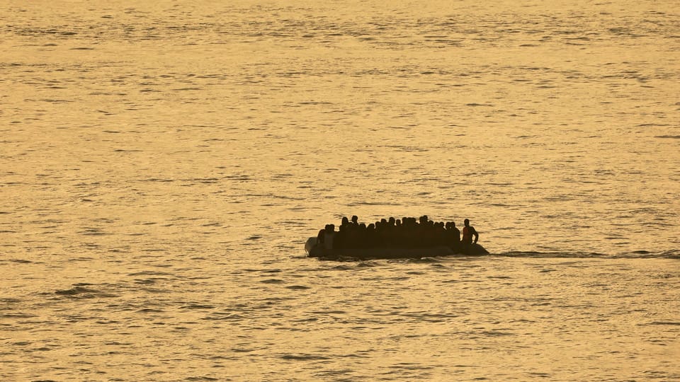 Eine Gruppe von Migranten auf einem Schlauchboot bei Sonnenaufgang im Meer.