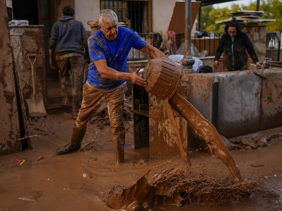 Person schüttet Schlamm aus einem Eimer, Umgebung voller Matsch.