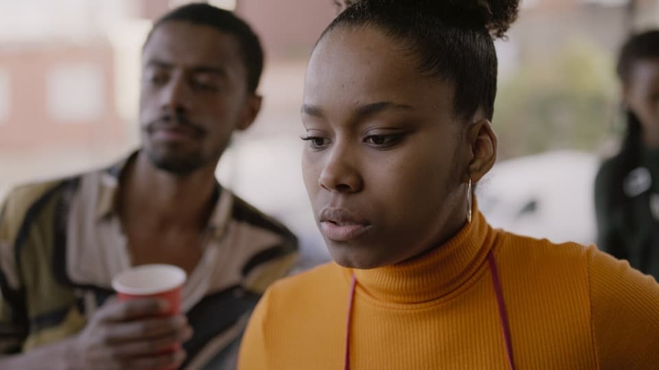 Eine schwarze junge Frau in orangem Rollkragenpullover schaut nachdenklick