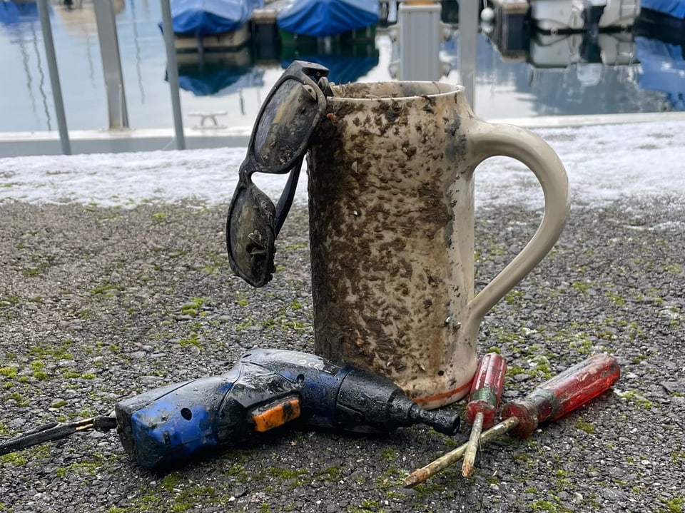 Aus dem Wasser gefischte Tasse, Sonnenbrille und Werkzeug.