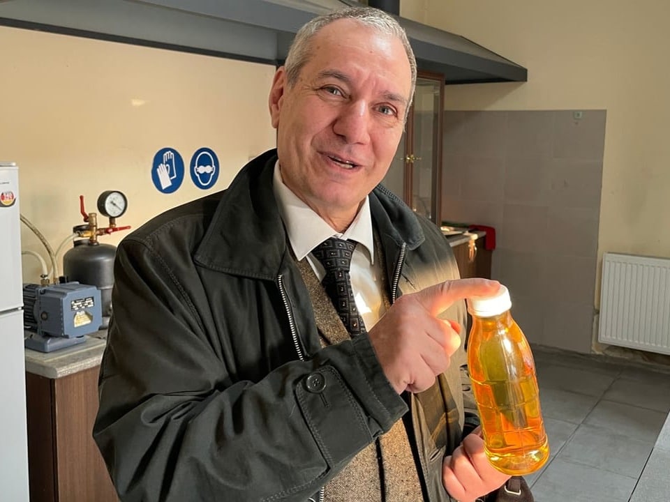 Mann zeigt auf Flasche mit gelber Flüssigkeit.