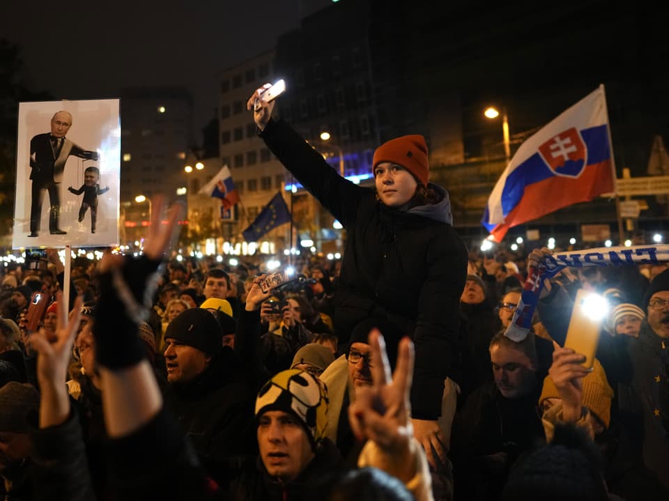 Menschenmenge bei Nacht mit slowakischer Flagge und Protestschildern.