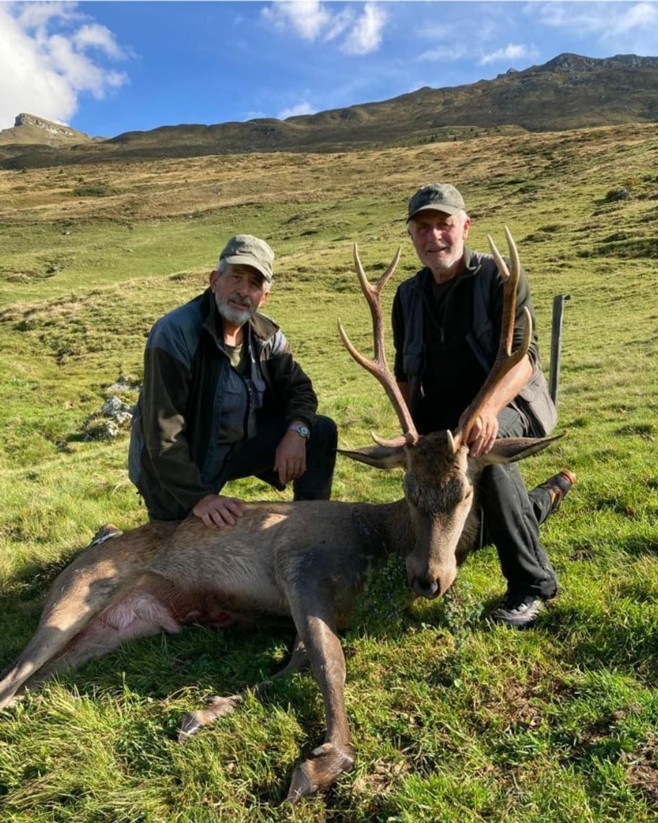 zwei Jäger mit erlegtem Hirsch auf einer Alpweide