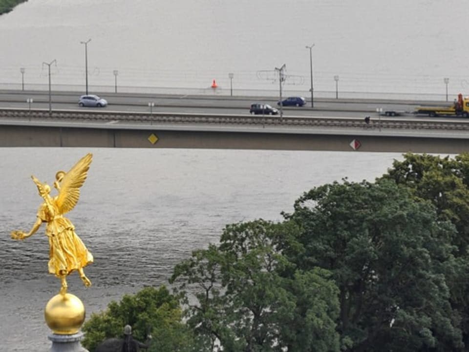 Goldene Statue vor einer Brücke über einem Fluss.