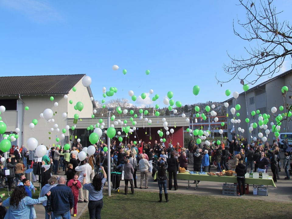 Menschen lassen grüne und weisse Luftballons steigen. 