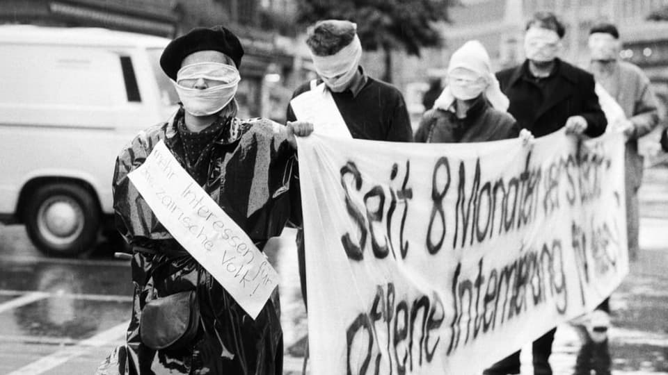 Demontranten mit verbundenem Gesicht und einem Transparent protestieren gegen eine Ausschaffung