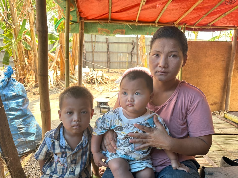 Mutter mit zwei kleinen Kindern sitzt in einer ländlichen Umgebung.