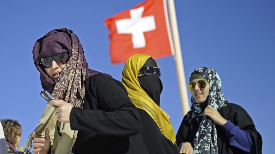 Drei Frauen mit Kopftüchern vor Schweizer Flagge.