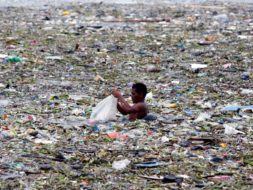 Mann fischt in der Bucht von Manila im Plastikabfall