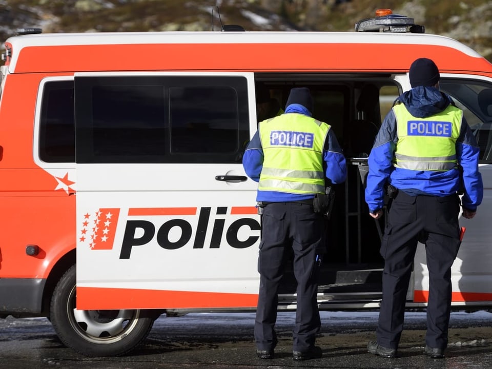 Walliser Polizisten stehen vor einem Einsatzwagen.