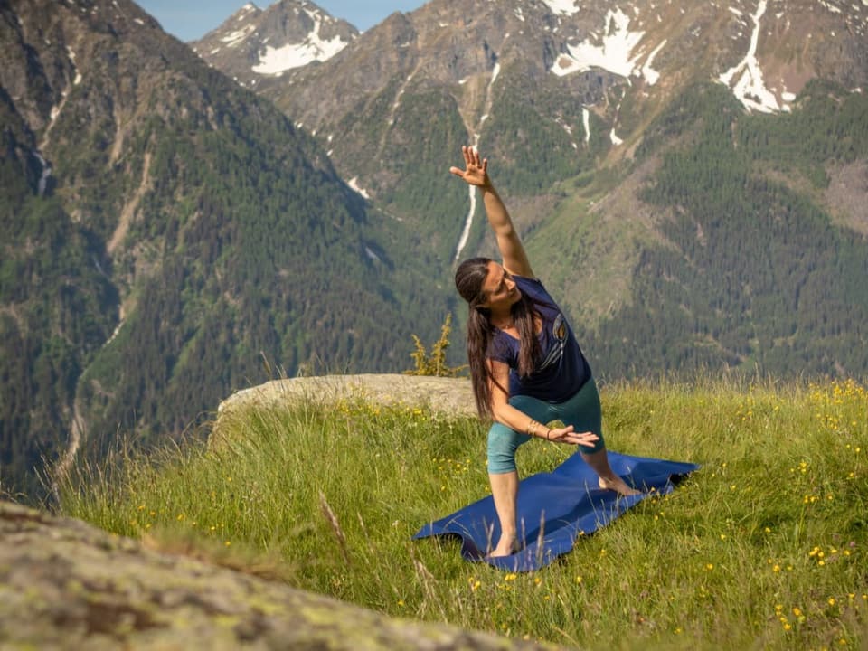 Yoga-Lehrerin Tiziana Dionisio macht auf der Wiese vor einer imposanten Bergkulisse eine Yoga-Pose.