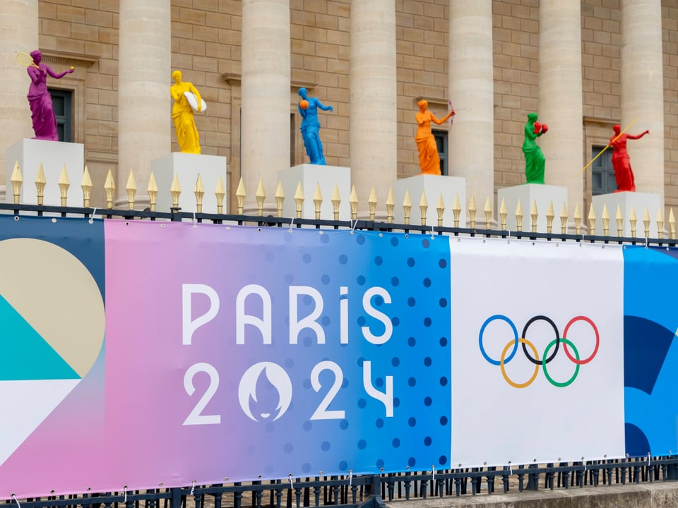 Plakate für die Olympischen Spiele 2024 in Paris vor einer Säulenfassade.