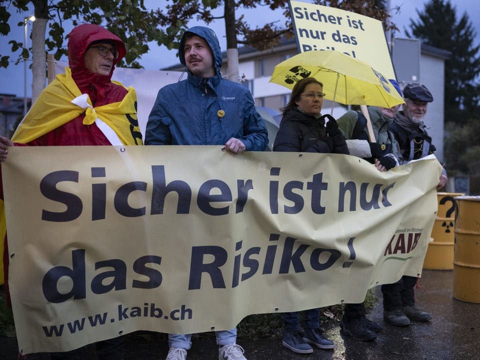 Gruppe protestiert mit Banner und Schildern im Regen.