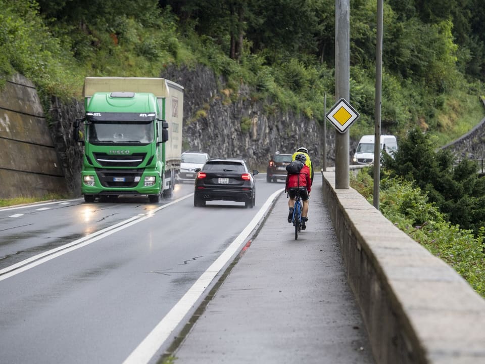 Radfahrer auf schmalem Weg neben einer Strasse mit LKW und Autos.