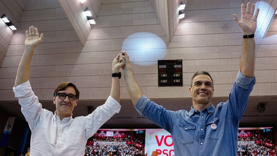 Zwei Männer halten bei einer Veranstaltung in einer Halle Hände hoch.