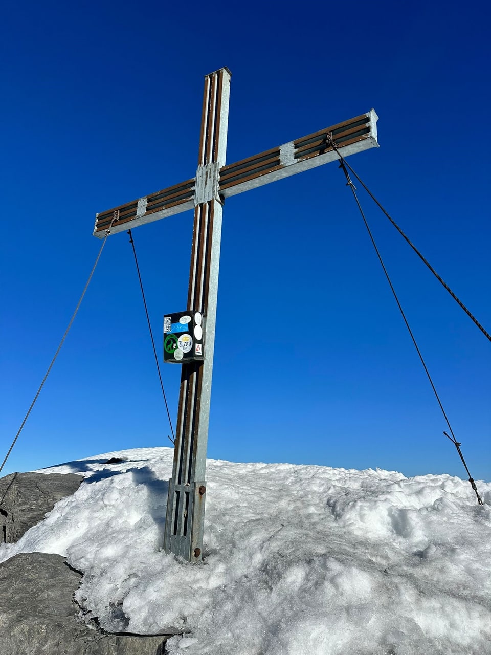 Gipfelkreuz auf schneebedecktem Berg vor blauem Himmel.