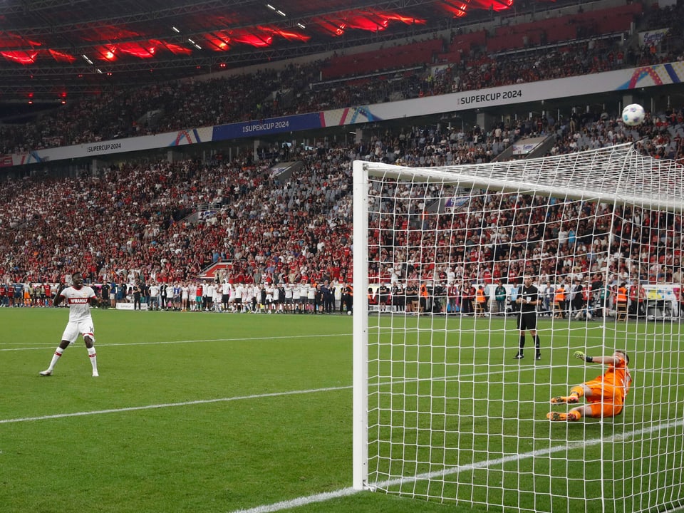 Fussballspieler schiesst Elfmeter, Torhüter taucht nach rechts, Tor im Stadion voller Zuschauer.