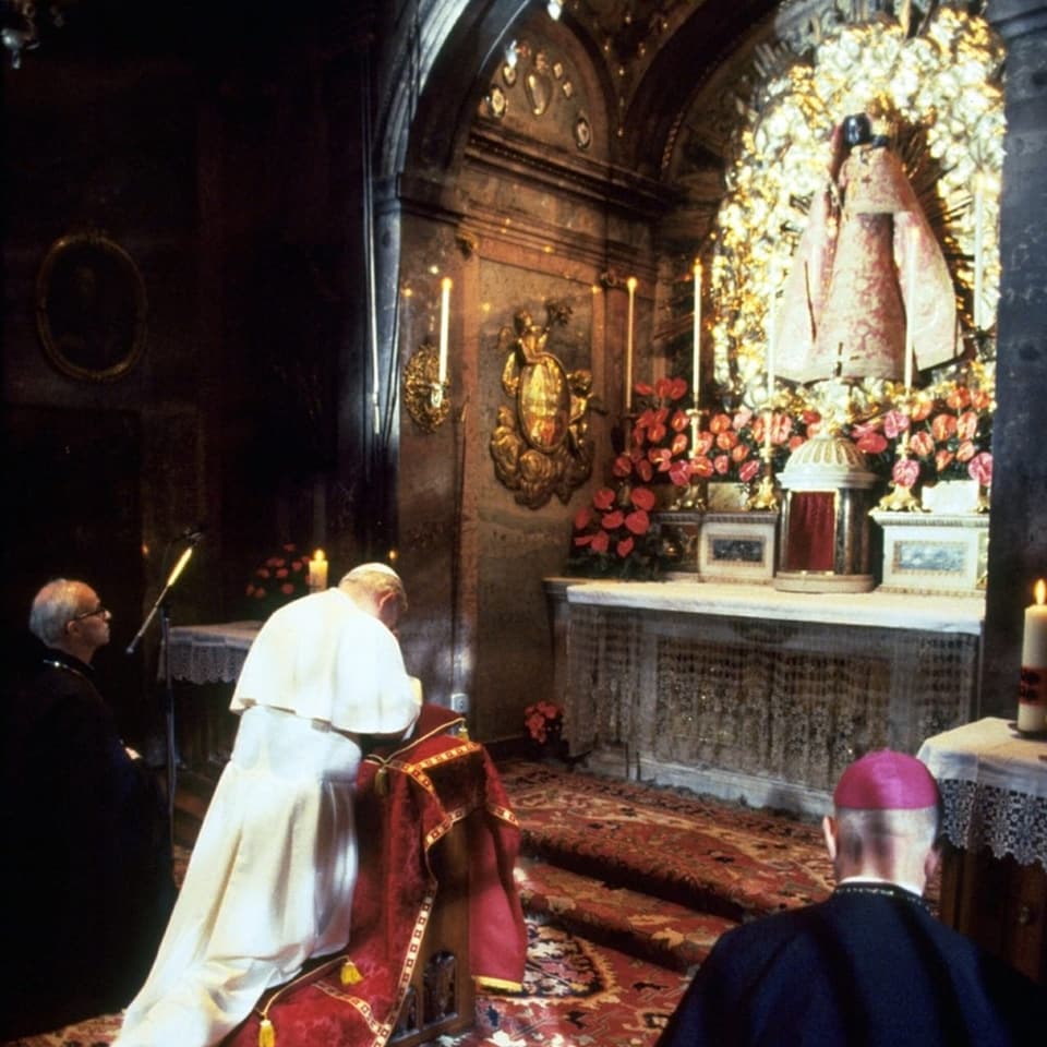 Personen beten vor Altar mit Marienstatue und Blumen.