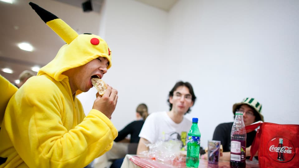 Ein junger Mann im Pikachu-Kostüm beisst in einen Hamburger.