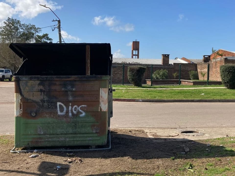 Müllcontainer mit Schriftzug Dios auf leerer Strasse.