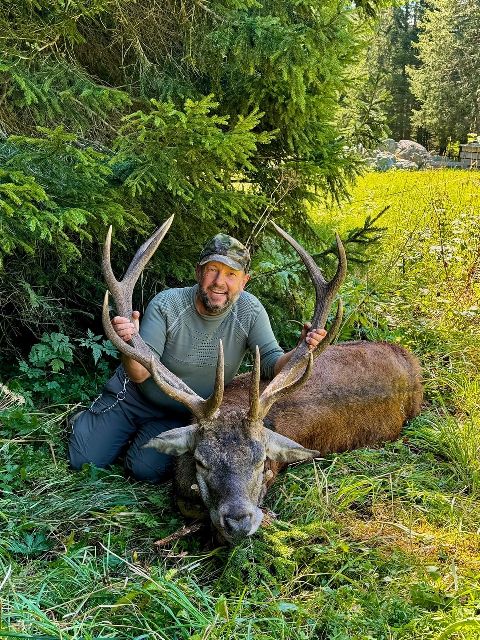 Mann posiert mit erlegtem Hirsch im Wald.