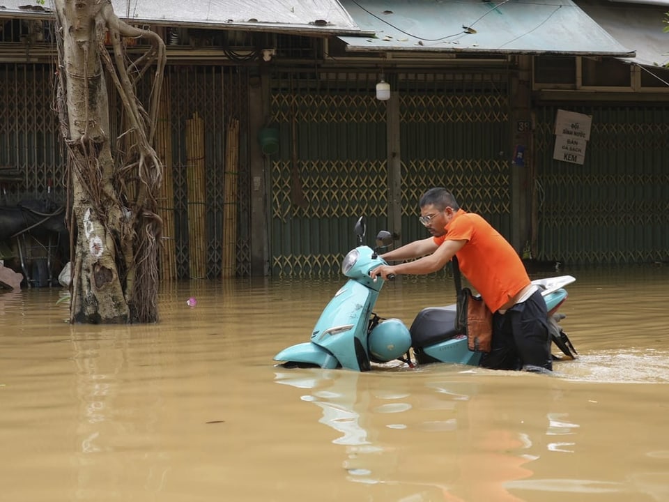 Mann schiebt Motorroller durch Hochwasser.