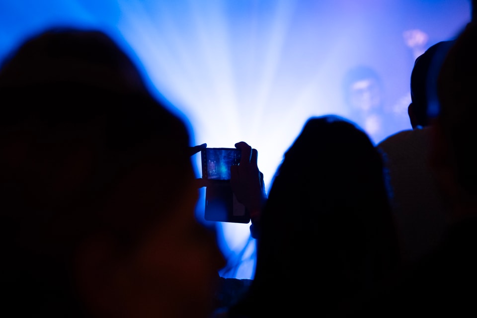 Person hält ein Smartphone vor einer blauen Bühnenbeleuchtung.