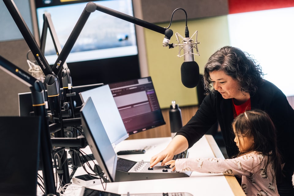 Frau und Kind im Radiostudio mit Computern und Mikrofon.